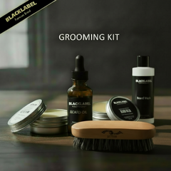 Blacklabel beard grooming kit arranged on a dark tabletop, including a beard oil dropper bottle, beard wash bottle, beard balm tins, a wooden beard brush, and a black branded ribbon banner in the corner.